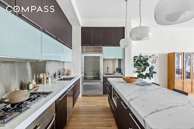 kitchen featuring light wood-type flooring, light stone counters, stainless steel appliances, pendant lighting, and sink