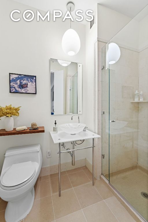 bathroom featuring tile patterned flooring, a shower with door, and toilet