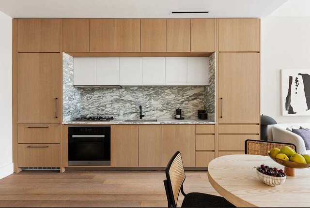 kitchen featuring stainless steel gas stovetop, decorative backsplash, a sink, and black oven