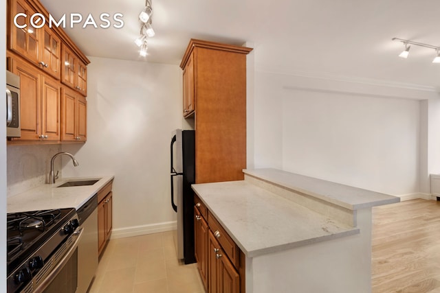 kitchen featuring stainless steel appliances, glass insert cabinets, a sink, light stone countertops, and a peninsula