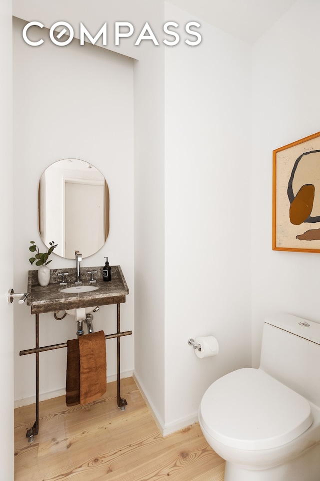 bathroom featuring toilet, wood finished floors, baseboards, and a sink