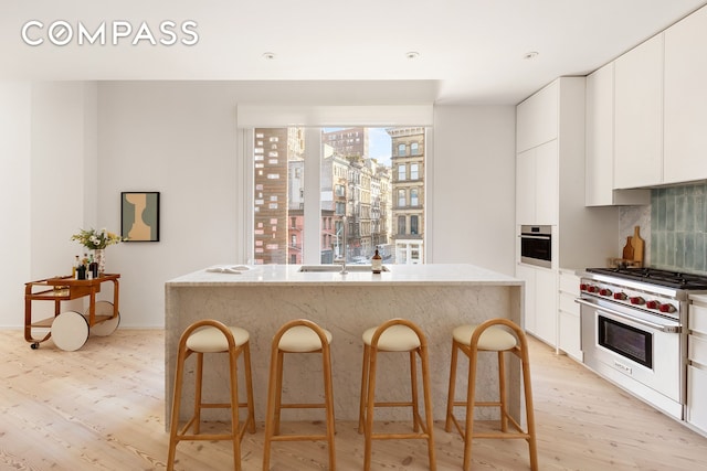 kitchen featuring a kitchen island with sink, light wood-style flooring, a kitchen breakfast bar, stainless steel appliances, and decorative backsplash