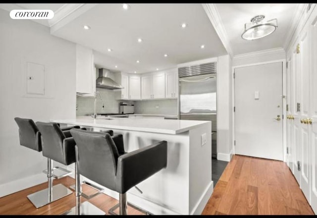 kitchen featuring sink, kitchen peninsula, white cabinetry, and wall chimney range hood