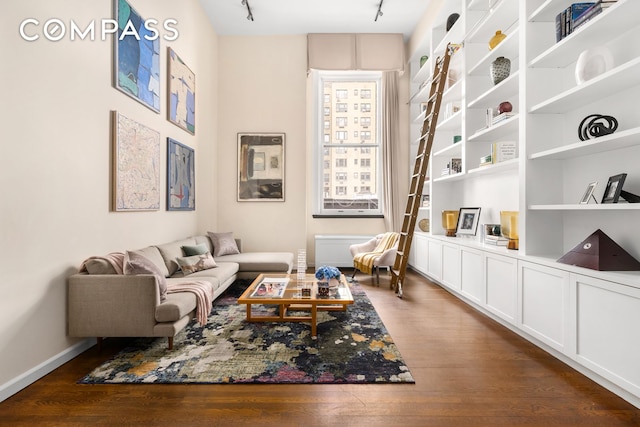 living area with baseboards, dark wood finished floors, built in features, and track lighting