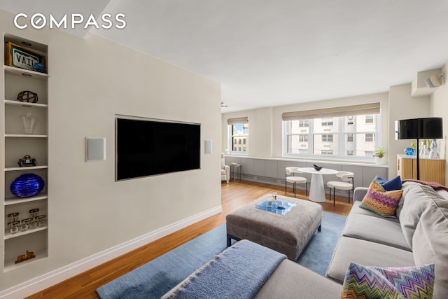 living area featuring built in features, baseboards, and wood finished floors