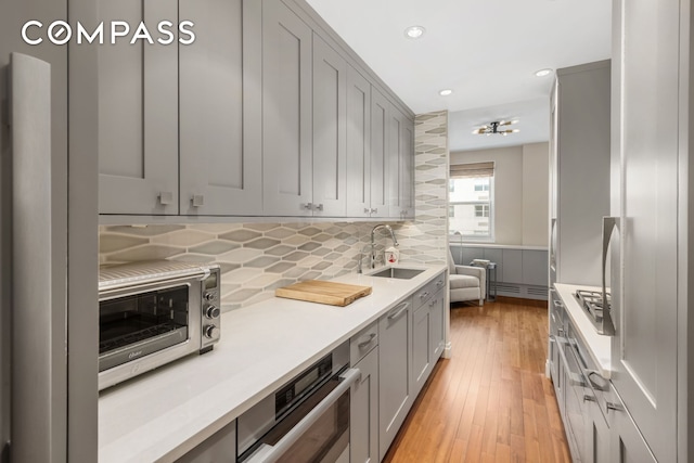 kitchen featuring gray cabinets, light countertops, a sink, and light wood-style flooring