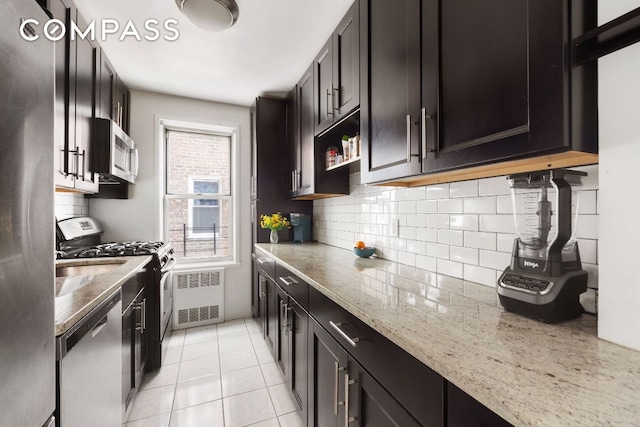 kitchen featuring appliances with stainless steel finishes, light stone counters, light tile patterned floors, and decorative backsplash