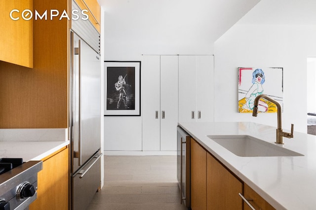 kitchen with built in fridge, light hardwood / wood-style flooring, sink, and stove