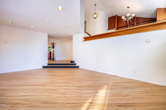 spare room with high vaulted ceiling, an inviting chandelier, and light hardwood / wood-style floors