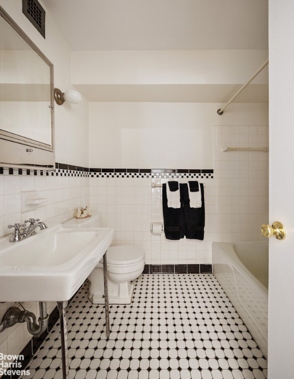 bathroom with shower / bathtub combination, toilet, a sink, visible vents, and tile walls