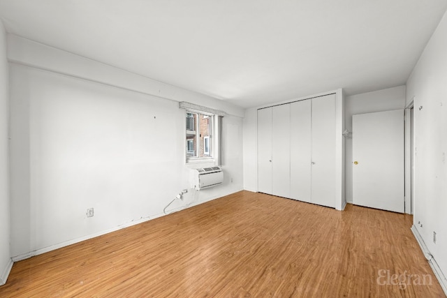 unfurnished bedroom with light wood-type flooring, a wall mounted AC, and a closet