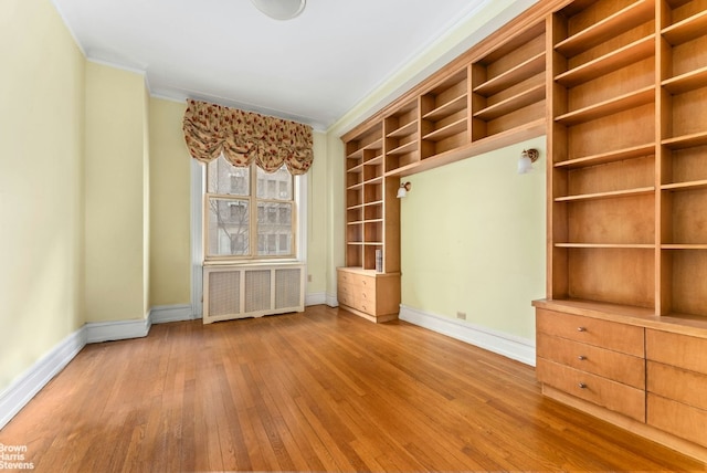 spare room with crown molding, radiator heating unit, light wood-type flooring, and baseboards