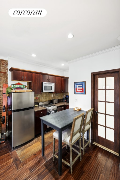 kitchen featuring crown molding, appliances with stainless steel finishes, dark wood-type flooring, and tasteful backsplash