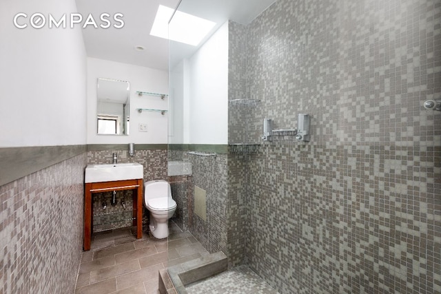 full bath with a walk in shower, a wainscoted wall, a skylight, vanity, and tile walls