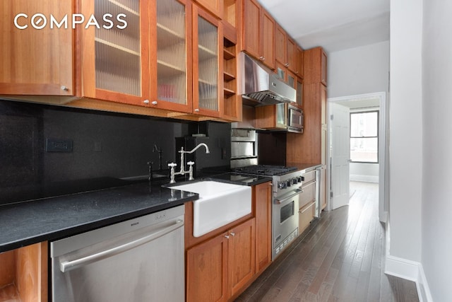 kitchen featuring under cabinet range hood, a sink, appliances with stainless steel finishes, dark countertops, and glass insert cabinets