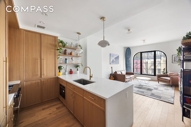 kitchen featuring light wood-type flooring, open floor plan, a sink, and a peninsula