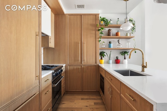 kitchen featuring high end stove, a sink, wood finished floors, visible vents, and open shelves