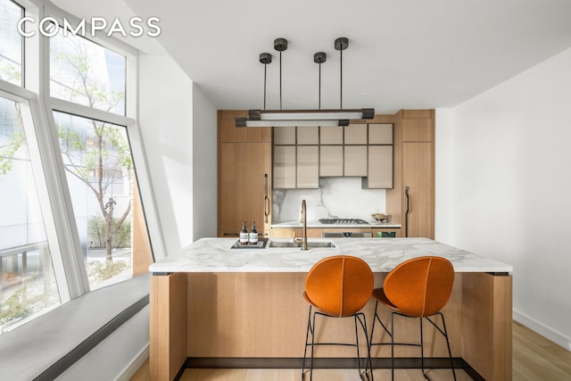 kitchen featuring light wood finished floors, tasteful backsplash, an island with sink, a breakfast bar area, and hanging light fixtures