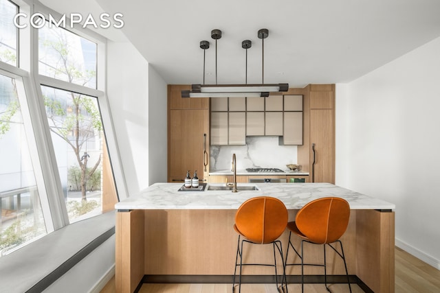 515 W 18th St Unit 210, New York City, NY 10011 - kitchen featuring decorative backsplash, light wood finished floors, a breakfast bar area, decorative light fixtures, and a kitchen island with sink