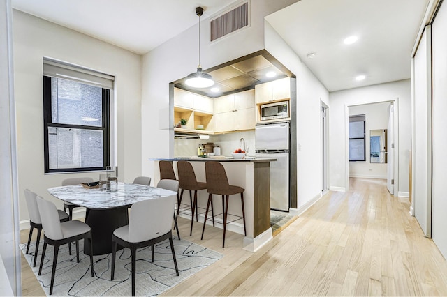 kitchen with light wood finished floors, stainless steel microwave, fridge, and visible vents