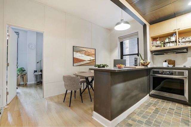 bar with hanging light fixtures, light wood finished floors, stainless steel oven, and tasteful backsplash