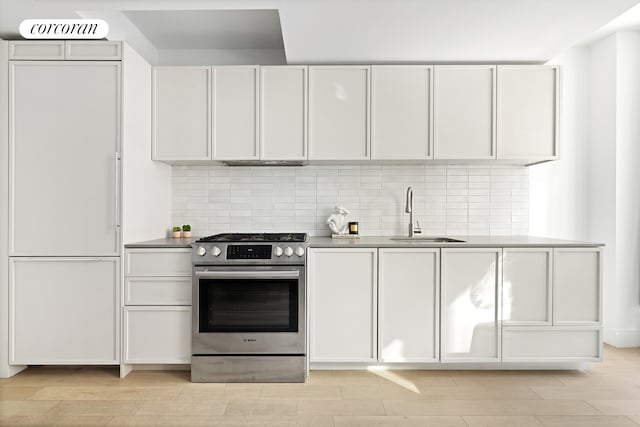 kitchen featuring stainless steel gas range oven, decorative backsplash, wood tiled floor, and a sink