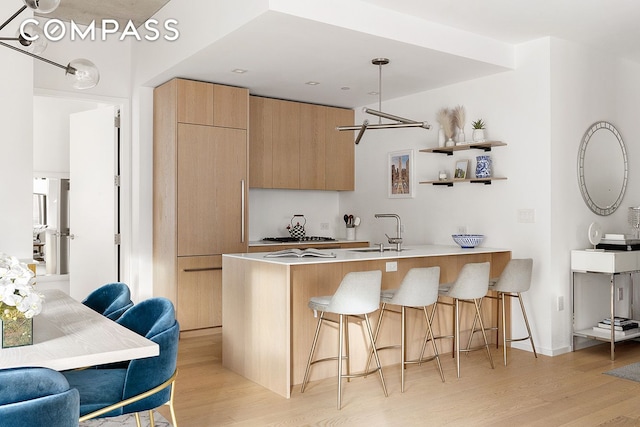 kitchen with a peninsula, a sink, light wood-style floors, a kitchen bar, and modern cabinets