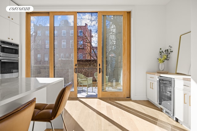 interior space with white cabinets, stainless steel double oven, a kitchen bar, light wood-type flooring, and beverage cooler