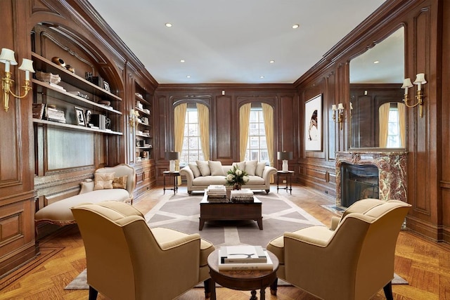 living area with built in shelves, wooden walls, a premium fireplace, crown molding, and light parquet floors