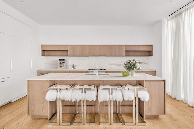 kitchen featuring open shelves, a kitchen island with sink, and light countertops