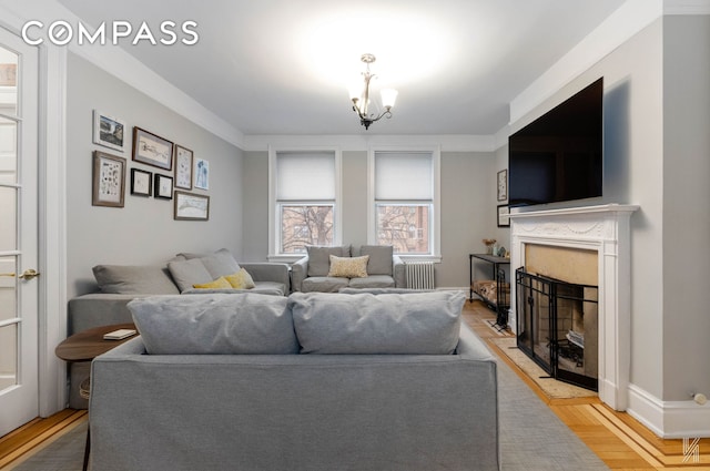 living area featuring a chandelier, a fireplace, baseboards, light wood-type flooring, and radiator heating unit