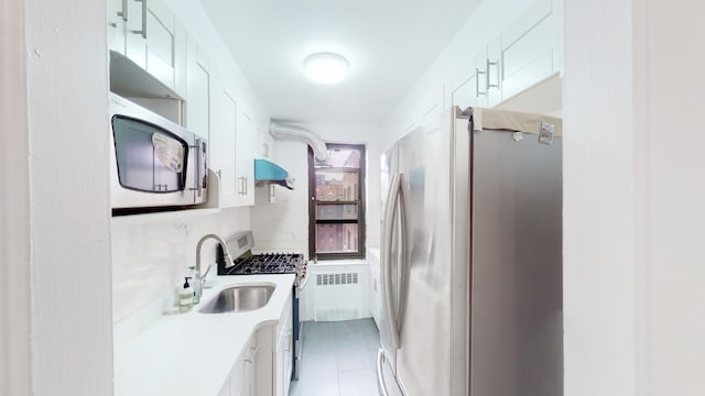 kitchen with appliances with stainless steel finishes, sink, radiator, and white cabinets