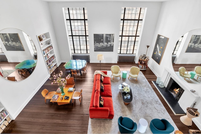 living room featuring dark wood-type flooring, arched walkways, a lit fireplace, and a towering ceiling