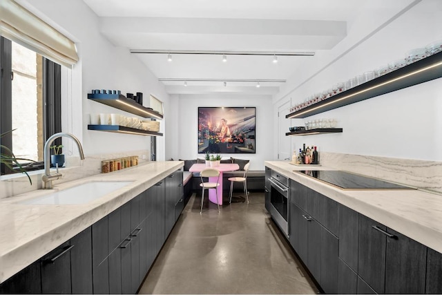 kitchen featuring track lighting, stainless steel oven, black electric stovetop, light stone countertops, and sink