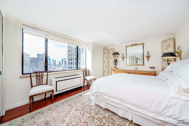 bedroom with radiator, baseboards, a city view, and wood finished floors