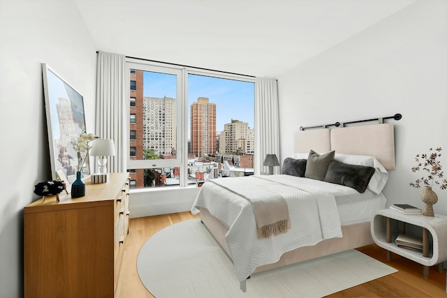 bedroom with a view of city and light wood-style flooring