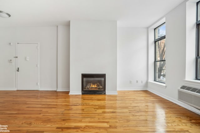 unfurnished living room with light wood-type flooring, a glass covered fireplace, a wall mounted air conditioner, and baseboards