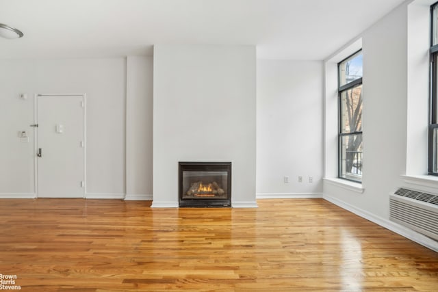 unfurnished living room featuring light wood finished floors, a glass covered fireplace, an AC wall unit, and baseboards