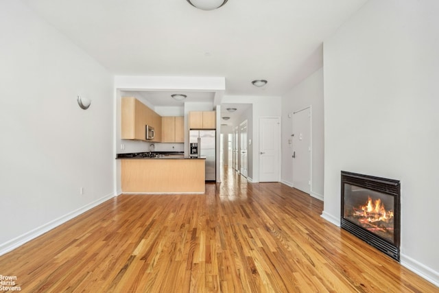 unfurnished living room with light wood-style floors, a glass covered fireplace, and baseboards