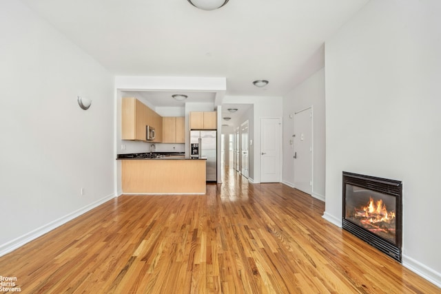 unfurnished living room featuring a glass covered fireplace, baseboards, light wood-style flooring, and a sink