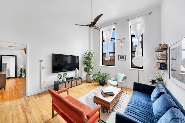 living area with baseboards, ceiling fan, and light wood finished floors