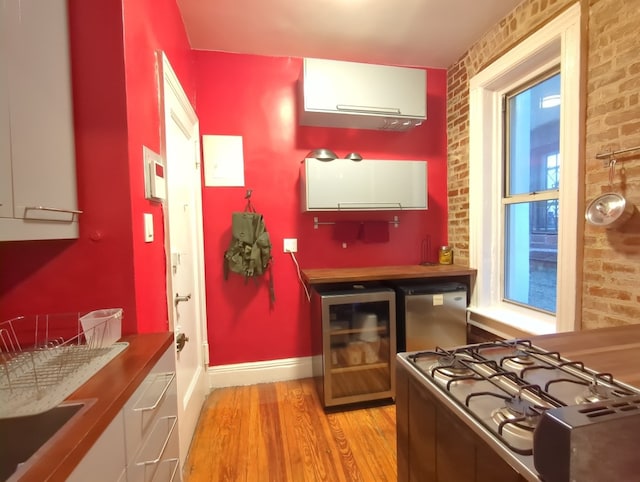 kitchen with brick wall, cooktop, wine cooler, fridge, and light wood-type flooring