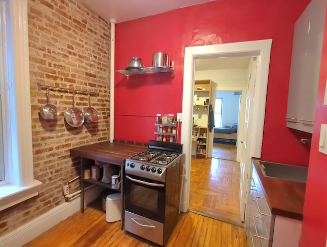 kitchen with stainless steel gas stove, brick wall, and wood finished floors