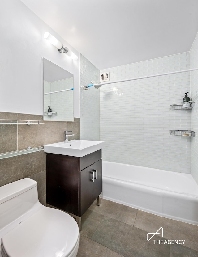 bathroom with tile walls, tub / shower combination, toilet, vanity, and tile patterned flooring