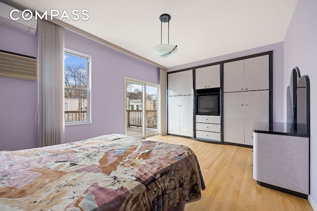 bedroom featuring access to outside, a wall mounted AC, and light wood-style floors