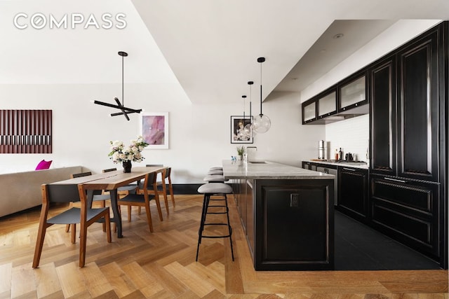 kitchen featuring an island with sink, decorative light fixtures, stone counters, a breakfast bar area, and light parquet floors