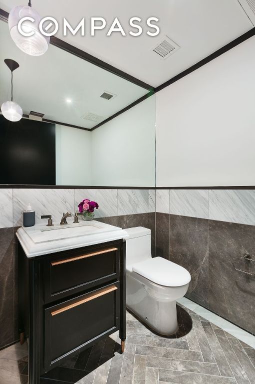 bathroom featuring toilet, tile walls, crown molding, and vanity