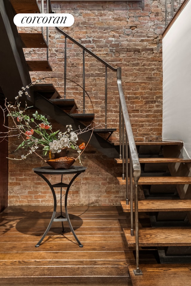 stairway with brick wall and hardwood / wood-style flooring