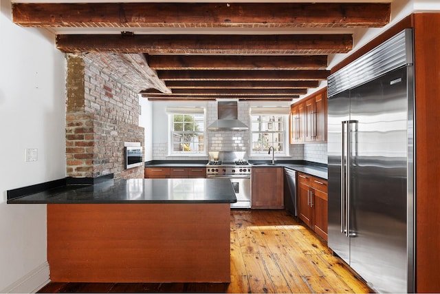 46 Perry St, New York City, NY 10014 - kitchen featuring light wood-style floors, beamed ceiling, wall chimney exhaust hood, a peninsula, and premium appliances
