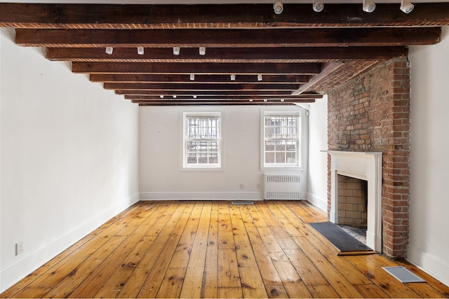 46 Perry St, New York City, NY 10014 - unfurnished living room featuring radiator, beamed ceiling, visible vents, a brick fireplace, and hardwood / wood-style flooring